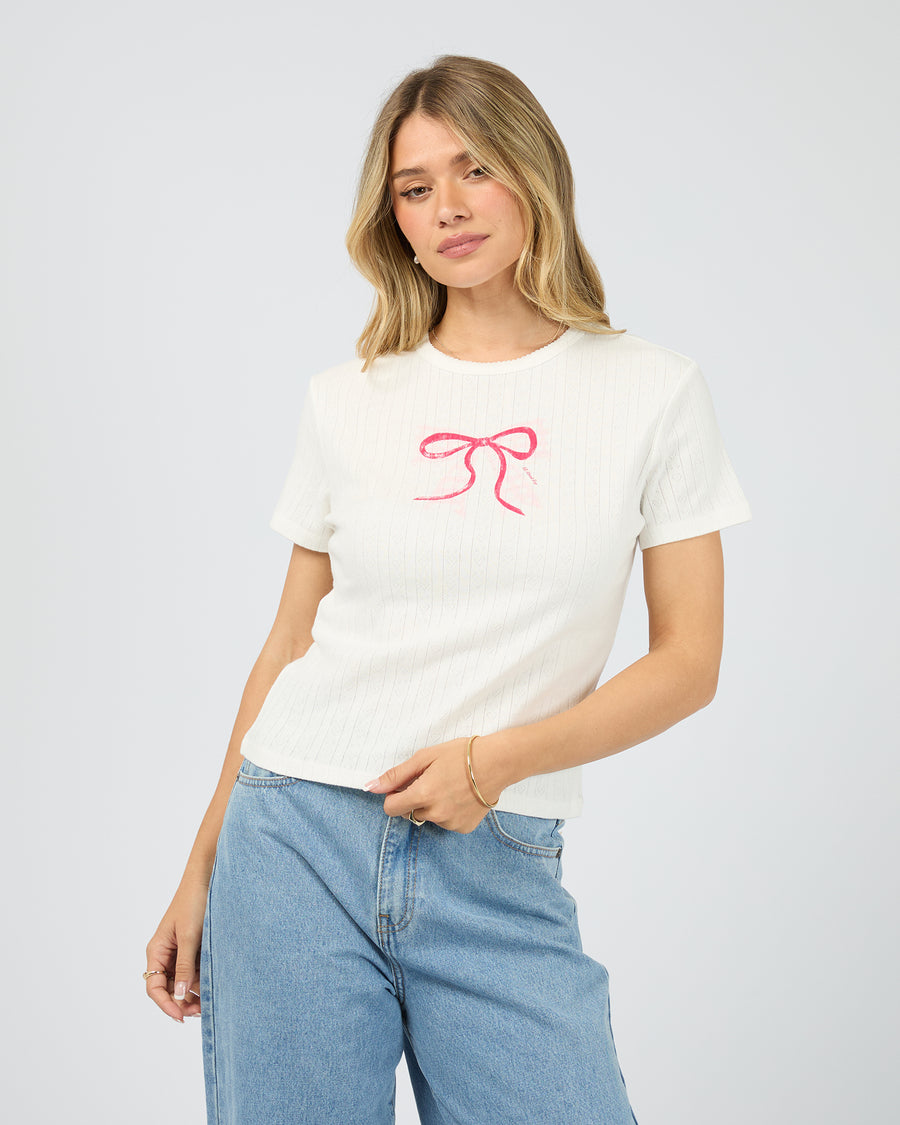 Alt Text: All About Eve Postal Baby Tee in Vintage White with pink bow detail, front view