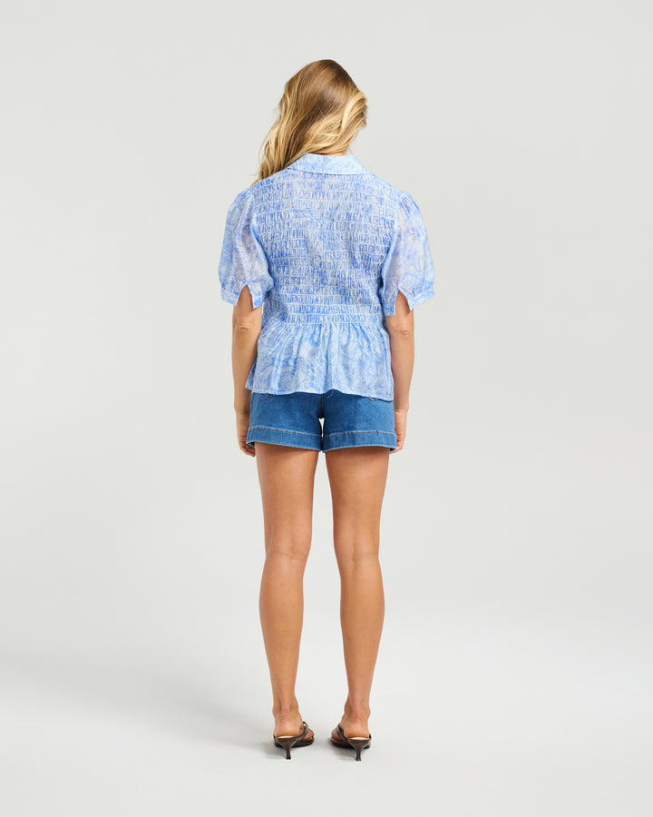Back view of Kiwi Country Kiki Blouse in Wildflower Sketch Blue paired with denim shorts.