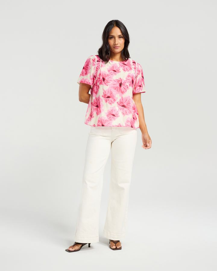 Front view of Kiwi Country Layton Top in Pink Bloom paired with white pants.